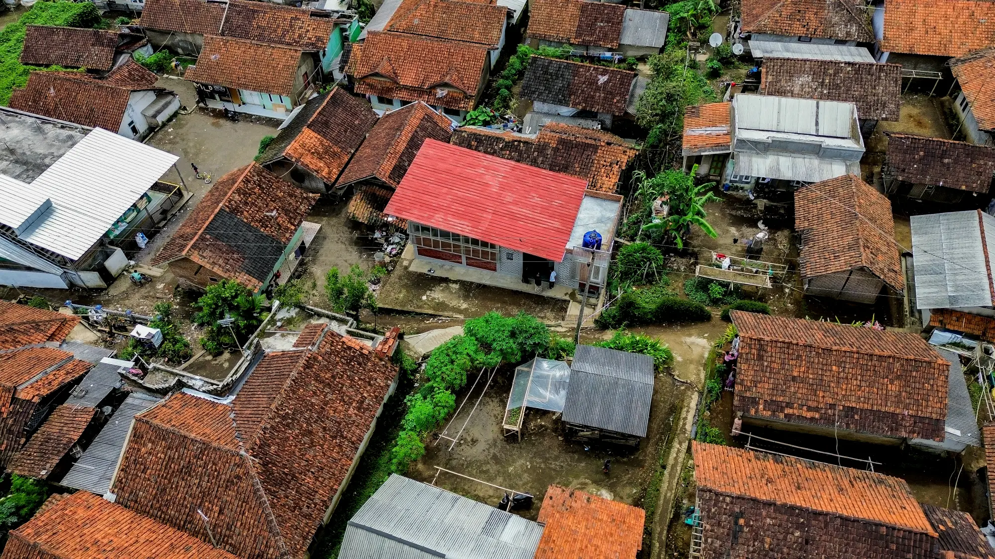 Aerial view of a village with various rooftops, lush greenery, and narrow pathways connecting houses in a traditional setting.