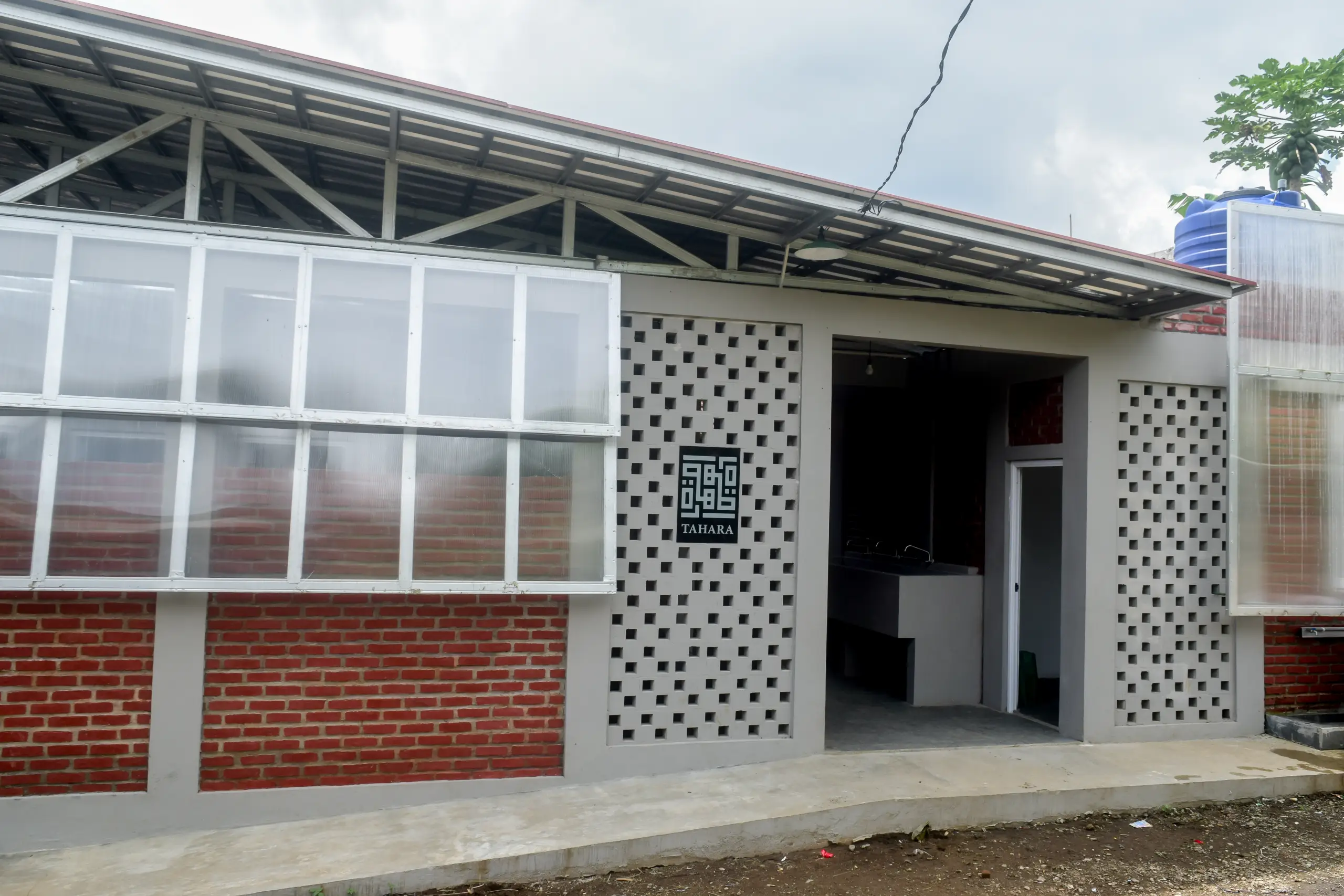 Exterior of a modern building featuring a brick wall, large windows, and the "TAHARA" sign, set against a cloudy sky.