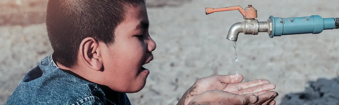 A child looks on as clean water flows from a tap into hands, highlighting the importance of water accessibility.