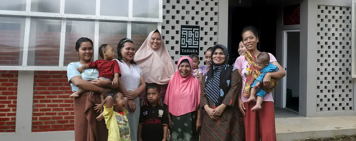A group of women and children stand together in front of a building with a sign that reads "TAHARA,".