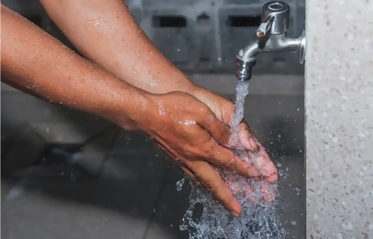 Two hands washed under a flowing faucet, water splashing as droplets cling to the skin, emphasizing hygiene and cleanliness.